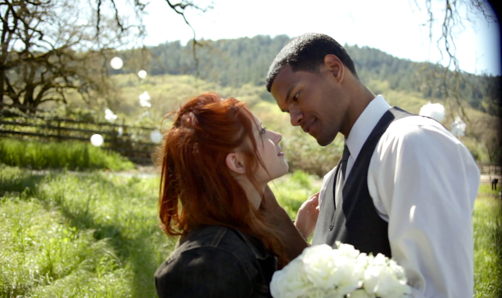 This image is a still from Sonja Kelly's feature film LOVE: As You Like It which was shot in 2012 by director of photography Adam Watson. It features a man and a woman getting married. They are looking into each other's eyes under a tree in a green field.